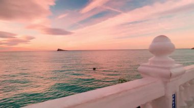 Benidorm 'daki Akdeniz bakış açısının ikonik balkonu boyunca yapılan manzara yürüyüşü, çarpıcı pembe ve turkuaz bir gündoğumu gökyüzünün altında şehrin ufuk çizgisini ve güzel kıyı şeridini gözler önüne seriyor.