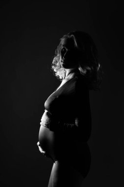 Genç ve güzel hamile bir kadın pembe arka planda duruyor.