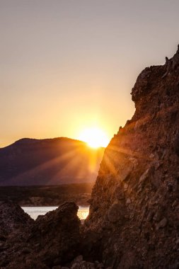 Sahilde güzel romantik bir gün batımı, dağın arkasında altın saat ve güneş, denizde dalgalar, poster ve arka plan.