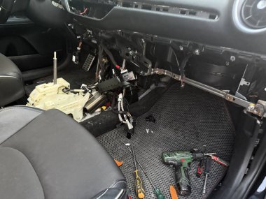 Arabanın içi gösterge paneliyle tamamen sökülmüş metal iskelet ve karmaşık elektrik kablolarını ortaya çıkarıyor. Kablosuz matkap ve tornavida içeren bir tamir sahnesi.