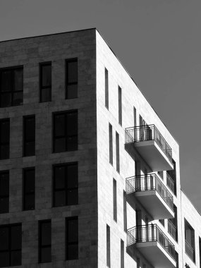Modern bir konut binasının köşesinde çarpıcı siyah beyaz bir fotoğraf. Kalıplı cephe, keskin geometrik çizgiler ve istiflenmiş balkonlar soyut, minimalist mimari tasarım yaratır..
