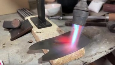 Yakından bakınca, meşale alevi metal bir plakayı ateş tuğlasında parlayan kırmızıya çeviriyor. Bir zanaat atölyesinde endüstriyel metalcilik, sertleştirme ve ilhak işlemleri.