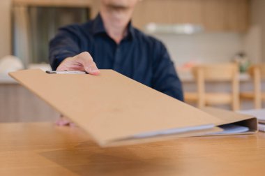 İş adamının elinin ofis masasındaki gizli bir klasöre uzanması, iş yerindeki aciliyet, veri işleme, belge yönetimi ve iş iletişimini sembolize eder.