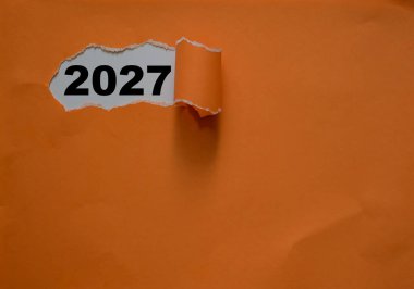 Yeni yıl iş planları ve yeni yıl çözümleri kavramında soyulmuş turuncu renkli kapaklı kağıt üzerinde 2027, kağıt üzerinde tipografik 2027 ile yeni yıl kavramı