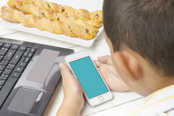 Child is looking mobile screen with background of laptop and breadstick