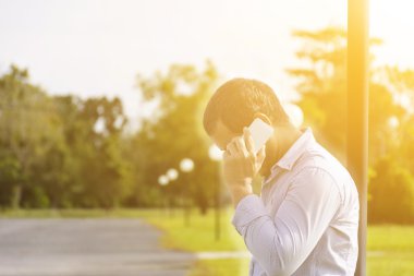 Arka plan doğa açık hava ve güneş görünümü ile mobil konuşan adam.