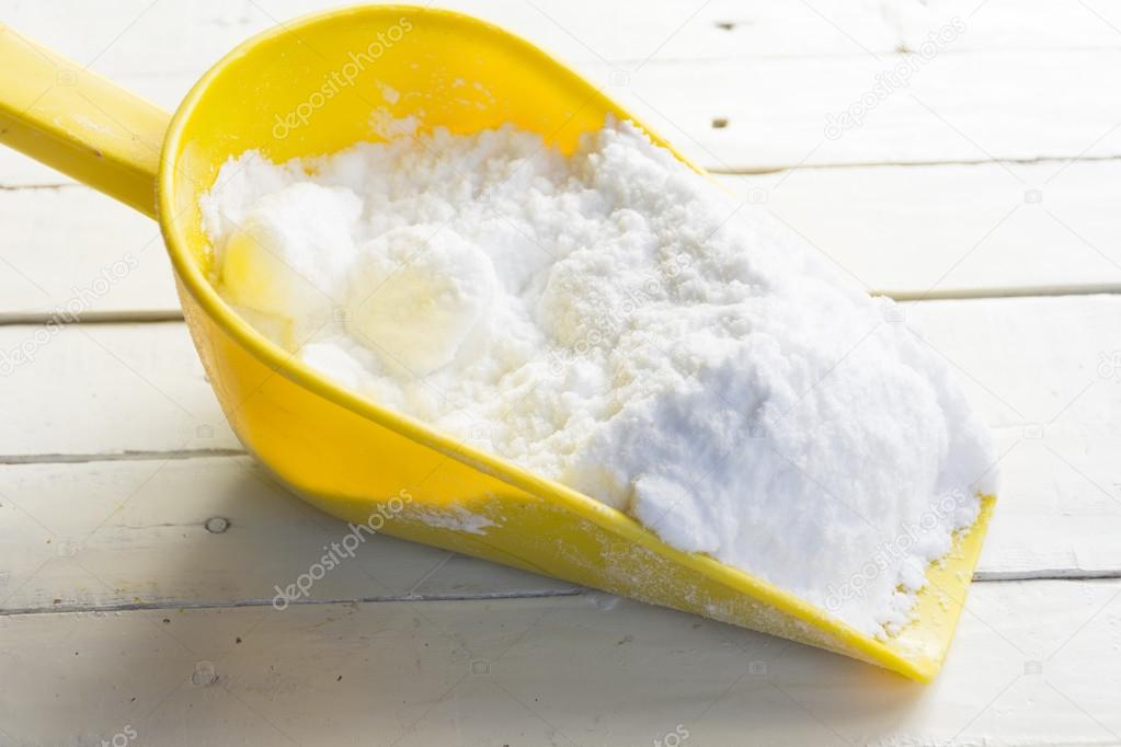 Dextrose in yellow shovel in hand on wooden white table.