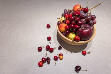 Tahta bir masanın üzerindeki dekoratif beyaz bir kasede taze üzüm ve erikleri yakın plan çek. Sığ alan derinliği sağlıklı beslenme ve iç tasarımı vurguluyor