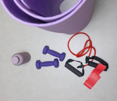 Dambıllar, direniş bantları ve gri arka planda fotokopi alanı olan bir yoga paspası da dahil olmak üzere ev fitness ekipmanlarının düz görünümü