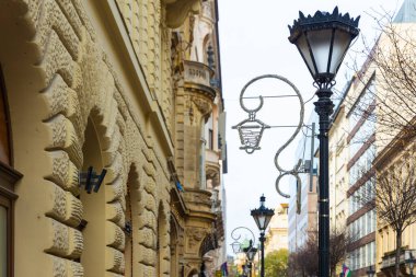 İnsanlar Macaristan 'ın Budapeşte kentindeki Bazilika Noel Pazarı yakınlarındaki tarihi bir bina kaldırımı boyunca süslü bir siyah sokak lambasının ve Noel süslemelerinin yanından geçtiler.