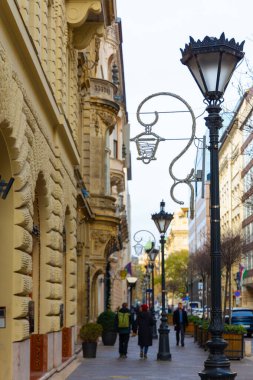 İnsanlar Macaristan 'ın Budapeşte kentindeki Bazilika Noel Pazarı yakınlarındaki tarihi bir bina kaldırımı boyunca süslü bir siyah sokak lambasının ve Noel süslemelerinin yanından geçtiler.