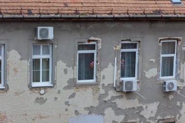 Dört pencere ve birkaç havalandırma ünitesinin bulunduğu yıpranmış gri bina duvarının yatay geniş açılı göz görüntüsü.