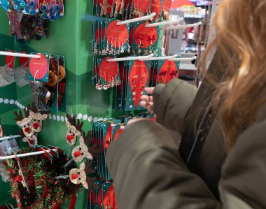 Yatay olarak geniş açılı göz merceği, tatil sezonu alışverişi sırasında, 26.11.2025 'te yeşil bir ekran standında bir kişinin ellerine uzanan neşeli küpeleri gösteriyor.