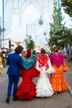 Fuengirola, Mlaga, İspanya. 12 Ekim 2025. Geleneksel flamenko elbiseli genç kadınlar geleneksel Ekim fuarı sırasında Fuengirola panayırında yürüyorlar..