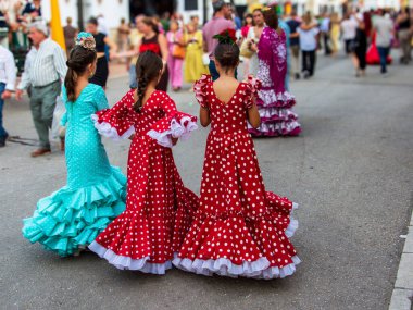 Fuengirola, Mlaga, İspanya. 12 Ekim 2025. Geleneksel flamenko elbiseli genç kadınlar geleneksel Ekim fuarı sırasında Fuengirola panayırında yürüyorlar..