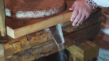 Eski Quern taş el değirmeni. Adam bir değirmen taşının yardımıyla tahılı un haline getiriyor. Değirmen taşının üzerinde erkek eli. Eski öğütücü taşlar ellerle çevrildi.
