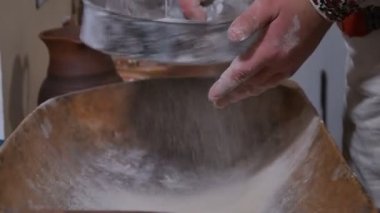 Baker fırın eldiveni içinden un seçiyor, ahşap bir kasede malzemeleri karıştırıyor, elleri yakın plan. Eski evde ekmek pişirmek için un pişiriyorum. Antik çağlarda fırınlanmış gıda ve ekmek yapma aşamaları.