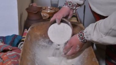 Kırsalda ekmek yapmanın eski bir yolu. Bir adam antika bir tabakta elleriyle hamuru karıştırıyor..