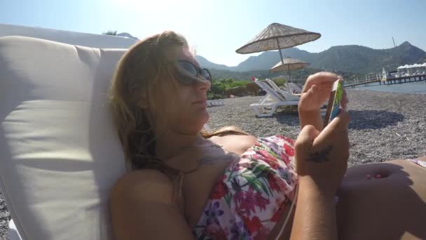 Kobieta robi coś z jego telefonu na plaży — Wideo stockowe