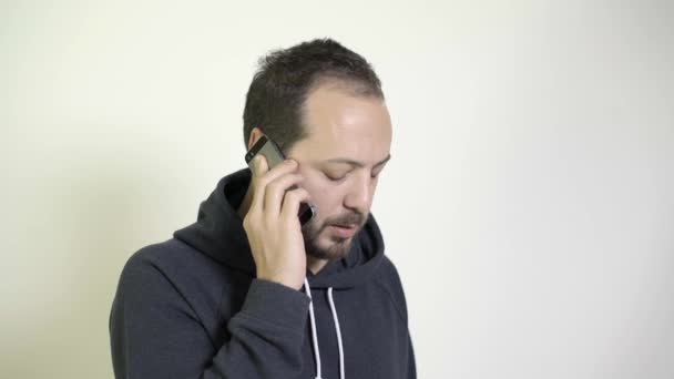 Мужчина разговаривает по телефону с другом, и он выглядит уставшим — стоковое видео