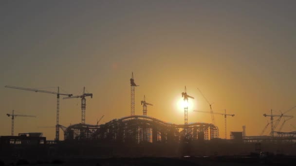 The rising sun appears from behind a silhouette building of the construction site - Time Lapse — Stock Video