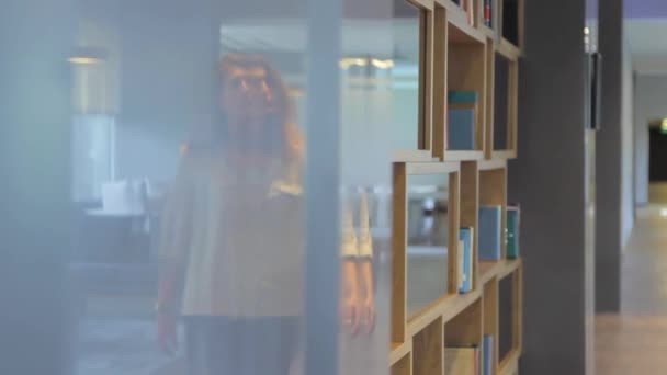 Aantrekkelijke vrouw plukken van een boek uit de boekenkast — Stockvideo