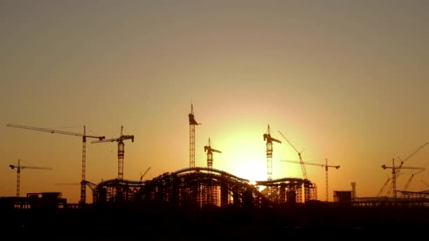 The rising sun appears from behind a silhouette building of the construction site - Time Lapse — Stock Video