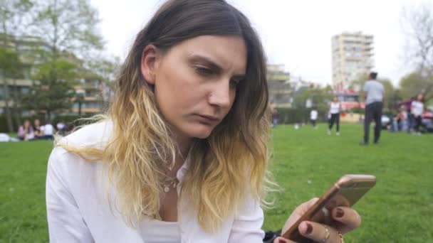 Молода жінка читає повідомлення по телефону в парку — стокове відео
