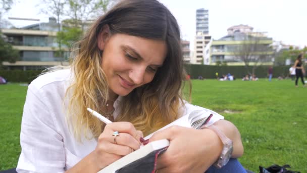 Mujer joven escribiendo algo en el cuaderno en el parque — Vídeo de stock