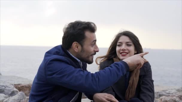 Casal jovem sentado ao lado do mar na pedra - Movimento lento — Vídeo de Stock