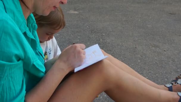 Mère et pâte sont assis sur le sol et dessine quelque chose dans la feuille de papier . — Video