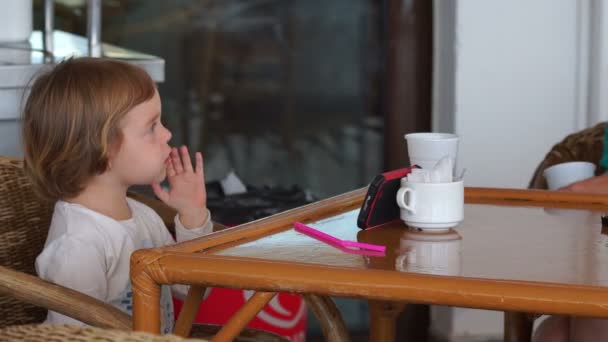 Kleines Mädchen sitzt im Café im Freien, sticht Mücke und benutzt Smartphone. — Stockvideo