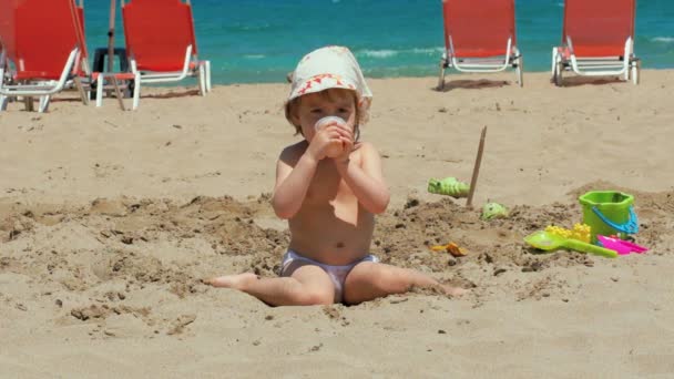 快乐的小女孩在沙滩上喝果汁. — 图库视频影像