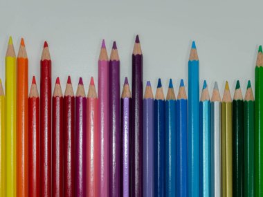 Büyüleyici, yakın plan, yatay çekim. Renkli kalemlerden oluşan canlı bir koleksiyon, dinamik bir gökkuşağı gradyanı ile beyaz bir arkaplana karşı dizilmiş. Kalemler değişik yüksekliklerle sunuluyor, ilginç dalgalanan bir baba yaratıyor.