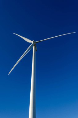Beyaz bir rüzgar türbininin dikey düşük açılı görüntüsü açık mavi gökyüzüne karşı kurulmuş. Temiz yenilenebilir enerji sürdürülebilirliği ve çevre kavramı.