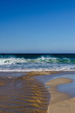 Islak kumsala vuran berrak mavi okyanus dalgalarının dikey görüntüsü. Su dokusu ve köpüğe odaklan. Yaz seyahati, doğa, sükunet ve tatil kavramı. Mükemmel kopyalama alanı.