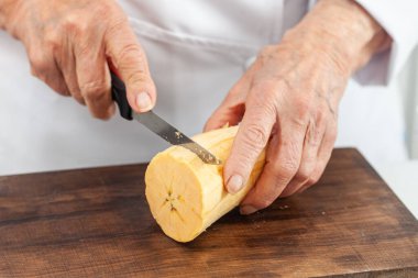 Olgun bir muz keserken, yaşlı bir kadının elleri yakındır.