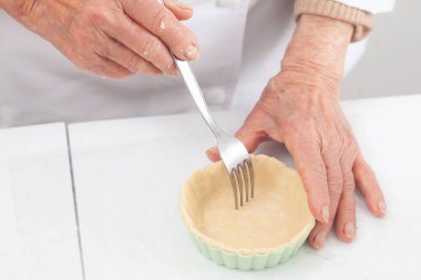 Kıdemli kadın lezzetli bir peynirli ve jambonlu tart için hamur hazırlıyor.
