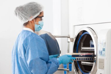 Genç bilim kadını, laboratuvar malzemelerini otoklavada sterilize ediyor.