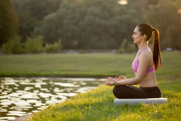 Genç sportif kız sabah çimenlerin üzerinde meditasyon yapıyor