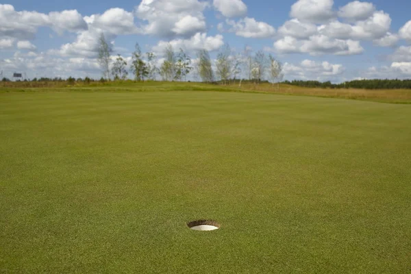 Golf hole on sunny golf course under blue sky with clouds