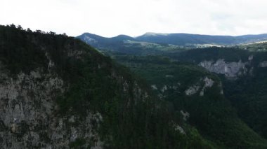 Stunning aerial drone footage of dramatic rocky cliffs rising above dense green forest. Perfect for themes of wilderness, geology, exploration, adventure travel, and untouched natural landscapes