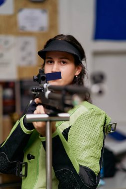 Genç bir kadın odaklanmış ve atış poligonuna nişan almış. Hassas bir atış sporuna katılıyor. Yeteneklerini ve kararlılığını gösteriyor..