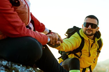 İki arkadaş gün batımında kayalık bir dağ yolunda yürürken birbirlerine yardım ediyorlar. Sıcak ışık onların neşeli ifadelerini ve dostluklarını vurguluyor..