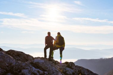 İki yürüyüşçü kayalık bir zirvede durup aşağıdaki büyüleyici manzaraya bakıyorlar. Güneş uzaklardan batıyor, vadiyi kaplayan bulutların üzerine sıcak bir parıltı saçıyor. Çift nefes kesici manzaranın keyfini çıkarıyor.