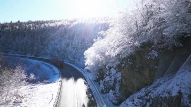 Donmuş ve buzla kaplanmış karla kaplı bir ormanı gösteren sinematik kış videosu gerçek bir cennet kışı yaratıyor. Arabalar ve kamyonlar geçerken buzlu ormanlık alandan geçen bir yol kontrastı vurguluyor.