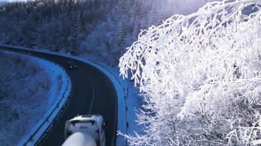 Donmuş ve buzla kaplanmış karla kaplı bir ormanı gösteren sinematik kış videosu gerçek bir cennet kışı yaratıyor. Arabalar ve kamyonlar geçerken buzlu ormanlık alandan geçen bir yol kontrastı vurguluyor.