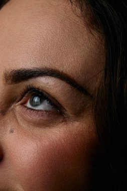 Bir kadının göz ve çevresindeki derinin detaylı bir yakın çekimi, dokulu cilt, tanımlanmış kaş, kirpik ve ince makyaj doğal ışık.
