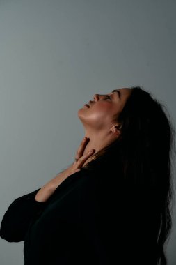 Gölgeli bir kadının zarif portresi, baş geriye doğru kavisli ve eli boynunda, karamsar ışıklandırma ile yoğunluk ve iç gözlem iletiliyor..