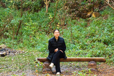 Genç bayan turist sosyal medya için akıllı telefon kaydını kullanarak park bankında oturuyor. Doğada rahatlamak, seyahatle dijital bağlantıyı ve açık hava deneyimini birleştirmek. Yüksek kalite fotoğraf